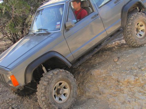 1995 Ford Bronco - A gray SUV navigates a steep, dusty incline with a person inside.