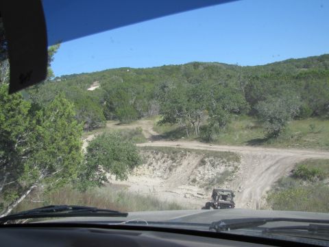 1995 Ford Bronco - A red Ford Bronco navigates a dirt road through a scenic, tree-lined landscape.