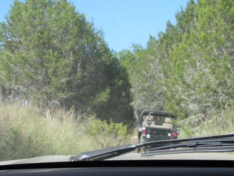 1995 Ford Bronco - An SUV is seen from inside a vehicle driving on a dusty, tree-lined road.
