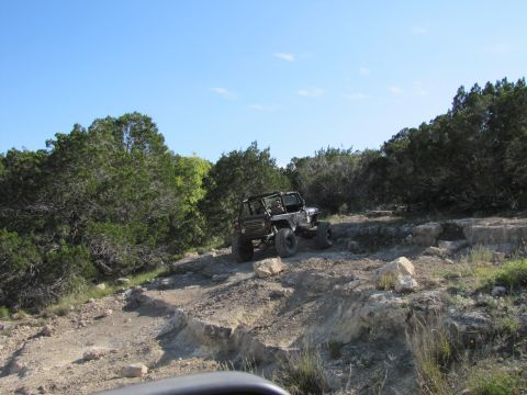 1995 Ford Bronco - A Jeep navigates a challenging rocky trail under a clear blue sky.