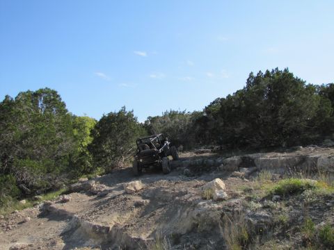 1995 Ford Bronco - An off-road vehicle navigates a challenging rocky terrain with dense foliage in the background.