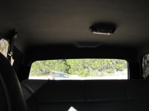 1995 Ford Bronco - View from inside a vehicle looking out the rear window at another white SUV parked outdoors.
