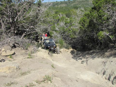 1995 Ford Bronco - A Jeep Wrangler tackles a challenging off-road path surrounded by dense vegetation and rocky terrain.