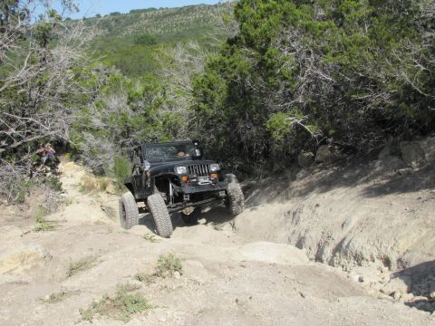 1995 Ford Bronco - Off-roading Jeep Wrangler navigates a challenging, dusty incline surrounded by arid vegetation.