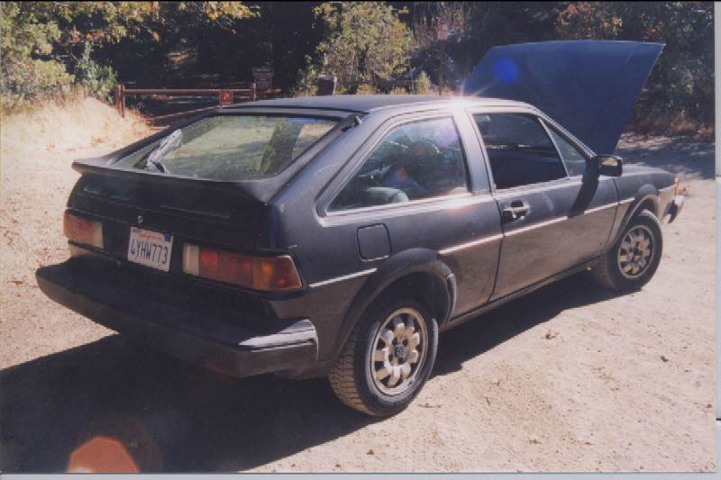 Rear 3/4 view of dark gray VW Scirocco hatchback with open rear hatch on dirt lot