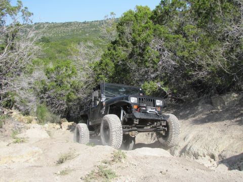 1995 Ford Bronco - Modified Jeep Wrangler tackling a challenging off-road course in a wooded, hilly area.