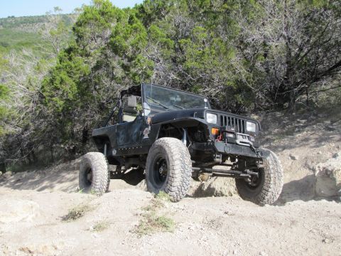 1995 Ford Bronco - A black Jeep Wrangler navigates a rocky, off-road trail surrounded by trees.