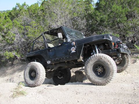 1995 Ford Bronco - This modified Jeep Wrangler is navigating a rocky, off-road trail with dense foliage in the background.
