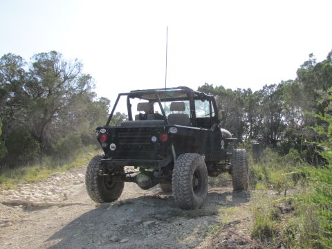 1995 Ford Bronco - This heavily modified off-road vehicle is seen from the rear on a dusty trail surrounded by trees.