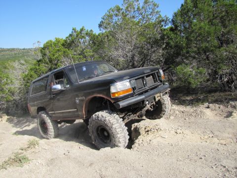 1995 Ford Bronco - This black SUV is shown off-roading on a sunny day with trees in the background.