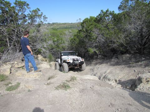 1995 Ford Bronco - A white Jeep Wrangler navigates a challenging off-road trail with a person observing the action.