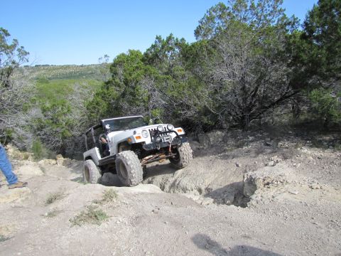 1995 Ford Bronco - A white Jeep Wrangler tackles a challenging off-road trail with steep inclines and rocky obstacles.