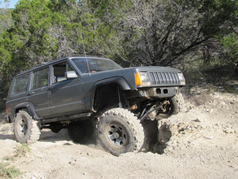1995 Ford Bronco - This Jeep Cherokee XJ is shown off-roading on a dirt trail with large tires and modified suspension.