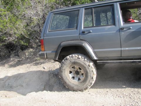 1995 Ford Bronco - A gray Jeep Cherokee XJ navigates an off-road trail, its large tires gripping the dirt.