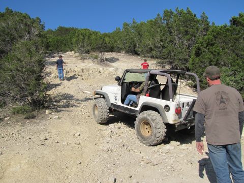 1995 Ford Bronco - A white Jeep Wrangler navigates a challenging rocky trail with spectators observing the off-road adventure.
