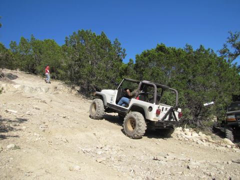 1995 Ford Bronco - A white Jeep Wrangler navigates a challenging off-road trail under a clear blue sky.