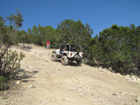 1995 Ford Bronco - A white Jeep Wrangler navigates a rocky off-road trail under a clear blue sky.