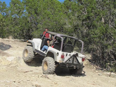 1995 Ford Bronco - A white Jeep Wrangler navigates a challenging off-road course with rocky terrain and dense foliage.