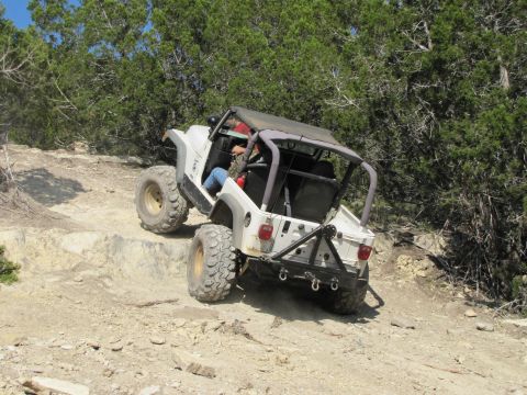 1995 Ford Bronco - A white Jeep Wrangler navigates a challenging off-road trail with steep inclines and rocky obstacles.
