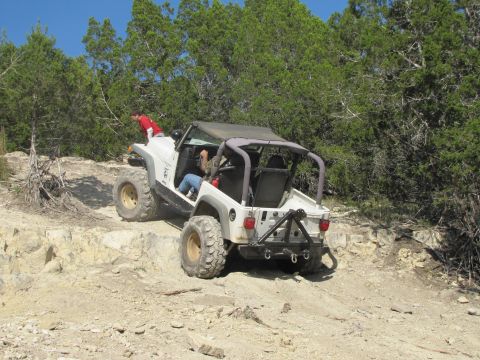 1995 Ford Bronco - A white Jeep Wrangler navigates a challenging rocky terrain under a clear blue sky.