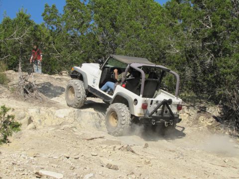 1995 Ford Bronco - A white Jeep Wrangler navigates a challenging off-road trail, with a person observing from a higher vantage point.