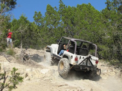 1995 Ford Bronco - A white Jeep Wrangler navigates a challenging rocky terrain under a clear blue sky.