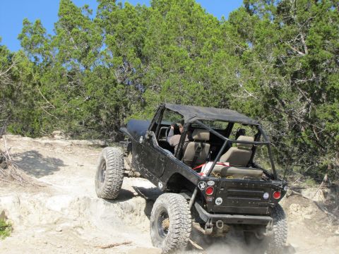 1995 Ford Bronco - A black Jeep Wrangler navigates a challenging rocky trail with a soft top and roll cage.