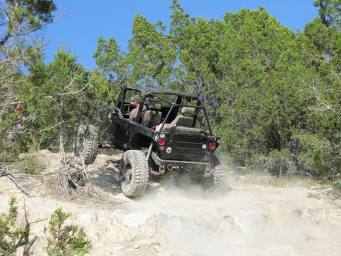 1995 Ford Bronco - Off-road vehicle kicks up dust while ascending a rocky, tree-lined trail.