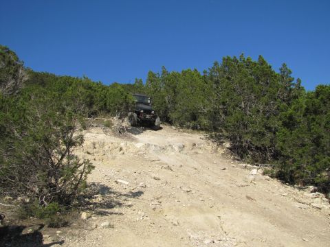 1995 Ford Bronco - A Jeep navigates a challenging off-road path under a clear blue sky.
