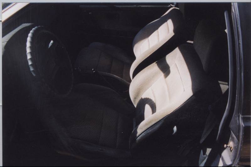 Black car interior with cloth bucket seats, passenger seat has cream insert
