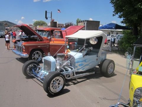 1991 Ford LTD Crown Victoria - A light blue hot rod with blue flames and a white convertible top is displayed at an outdoor car show, alongside other vehicles.