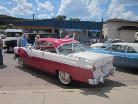 1991 Ford LTD Crown Victoria - A two-tone red and white 1956 Ford Fairlane Crown Victoria is displayed at a car show with an American flag on its trunk.