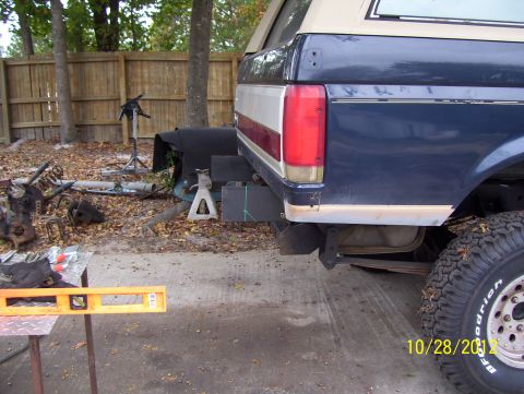 1990 Ford Bronco - A blue Ford Bronco is parked outdoors with its rear quarter panel visible, surrounded by various automotive parts and tools.