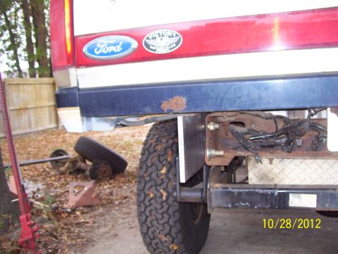 1990 Ford Bronco - Rear view of a 1990 Ford Bronco, showing the bumper, tire, and part of the body. The vehicle appears to be undergoing maintenance.