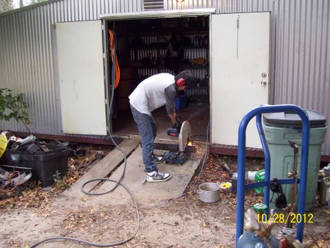1990 Ford Bronco - A person is using a chop saw to cut metal in front of an open shed door.