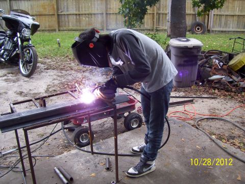 1990 Ford Bronco - A person welds a metal frame in a yard with a motorcycle parked nearby.