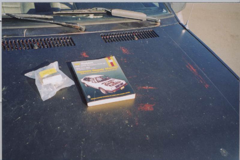 Haynes VW repair manual and bagged part resting on a faded dark-blue car hood