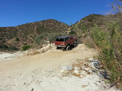 1978 Ford Bronco - A red 1978 Ford Bronco navigates a steep, dusty trail in a mountainous, arid landscape.