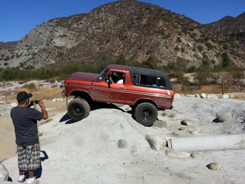 1978 Ford Bronco - A 1978 Ford Bronco navigates a rocky off-road course under a clear blue sky.