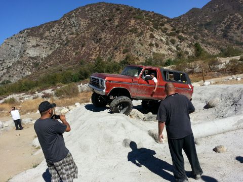 1978 Ford Bronco - A man films a lifted orange Ford Bronco navigating a rocky off-road trail in a mountainous area.