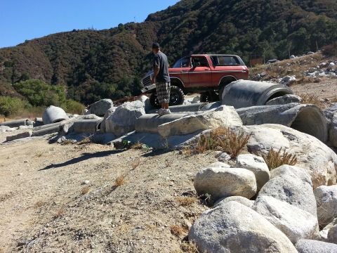 1978 Ford Bronco - A red 1978 Ford Bronco is positioned on a rocky landscape, with a person standing nearby on a concrete pipe.