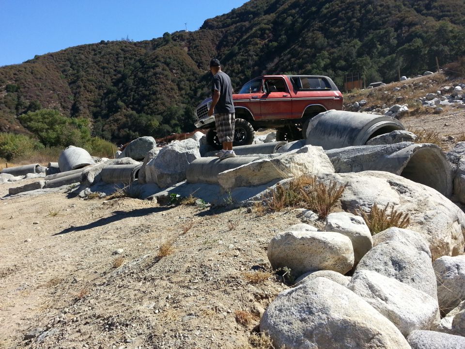 Red 1978 Ford Bronco parked on rocky terrain with a person standing on a concrete pipe