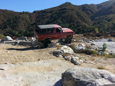 1978 Ford Bronco - A red 1978 Ford Bronco is shown off-roading over large rocks in a dry, mountainous area.