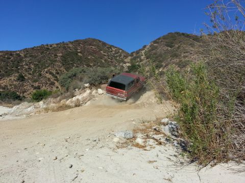 1978 Ford Bronco - A red and black 1978 Ford Bronco navigates a dusty, off-road trail with hills in the background.
