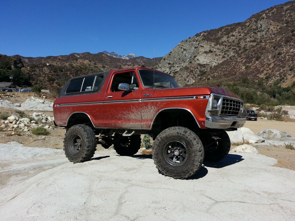 Orange 1978 Ford Bronco with large tires parked on a rock in a dry, mountainous area