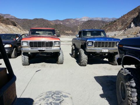 1978 Ford Bronco - Two lifted 1978 Ford Broncos are parked in a dusty, mountainous area under a clear blue sky.