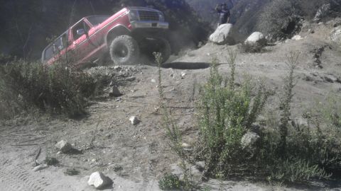 1978 Ford Bronco - Red pickup truck navigates a steep dirt path, kicking up dust.