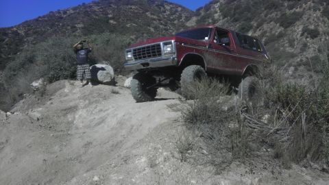 1978 Ford Bronco - A red 1978 Ford Bronco navigates a steep, rocky incline on a sunny day.