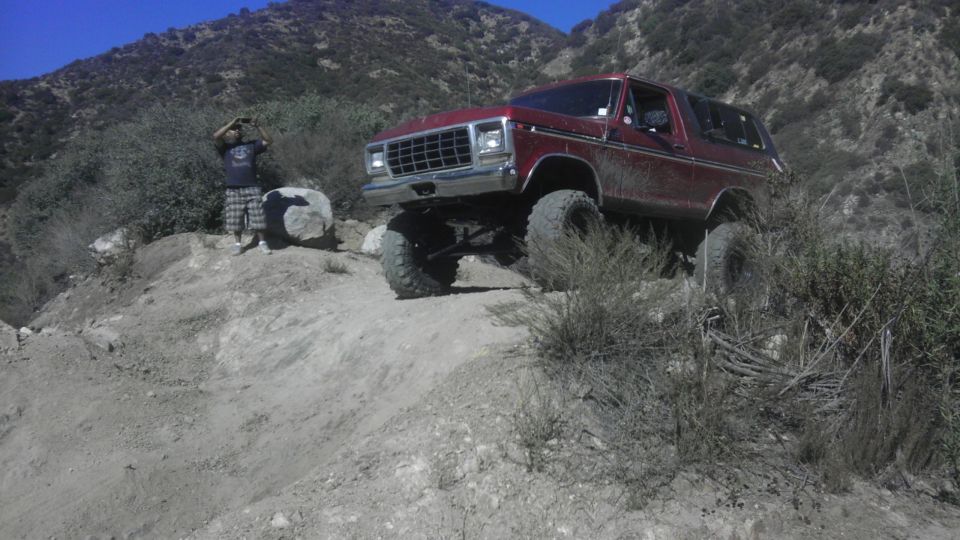Red 1978 Ford Bronco climbing a dirt hill with a person standing on the side