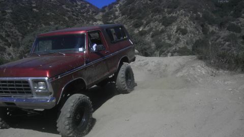 1978 Ford Bronco - A red 1978 Ford Bronco navigates a dusty mountain trail with its suspension lifted.